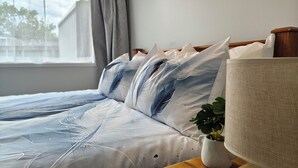 A neatly made bed with a blue and white patterned bedspread, a bedside lamp, and a smartphone on a wooden nightstand. -  Kozy Kottage, Near Hospital & Perfect for Families  (Hamilton)