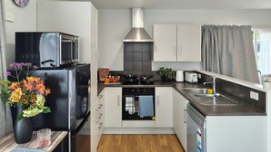 A modern kitchen with a microwave, oven, and dishwasher. There is a clock on the wall and a vase with flowers on the counter. -  Kozy Kottage, Near Hospital & Perfect for Families  (Hamilton)