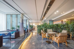 A modern hotel lobby with a pool table, seating area, and abundant indoor plants.
