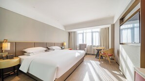 Een hotelkamer met een groot bed, nachtkastjes, een bureau, een stoel en een raam met gordijnen.
