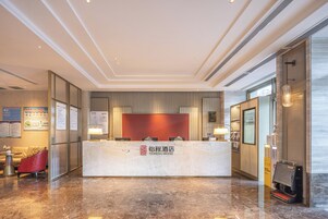 A hotel reception area with a marble floor, a reception desk, and a red accent wall.