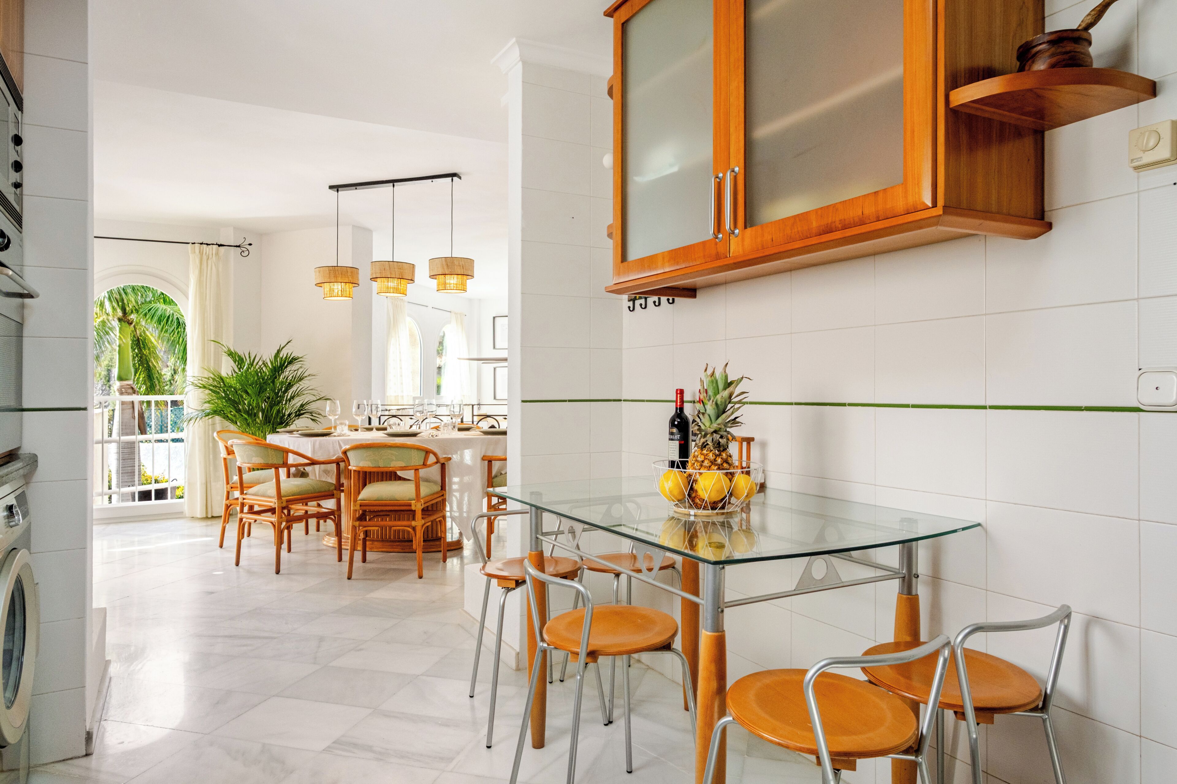 A modern kitchen with a glass dining table, wooden chairs, and a wooden cabinet.