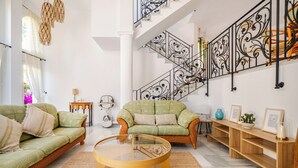 A spacious living area with a high ceiling, a staircase with ornate railings, and two green sofas. - The Oasis Beachfront Villa (Almuñécar)