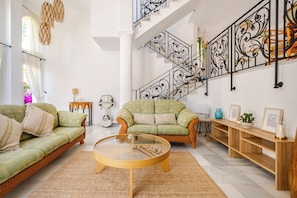 Ein großzügiger Wohnbereich mit hoher Decke, einer Treppe mit aufwendiger Geländerkonstruktion und zwei grünen Sofas.