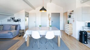 Une cuisine moderne avec une table à manger, des chaises, un luminaire suspendu, un canapé et une petite plante.