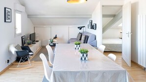 Une pièce moderne de style loft, comprenant une table à manger, des chaises, un luminaire suspendu noir, un canapé et un lit.