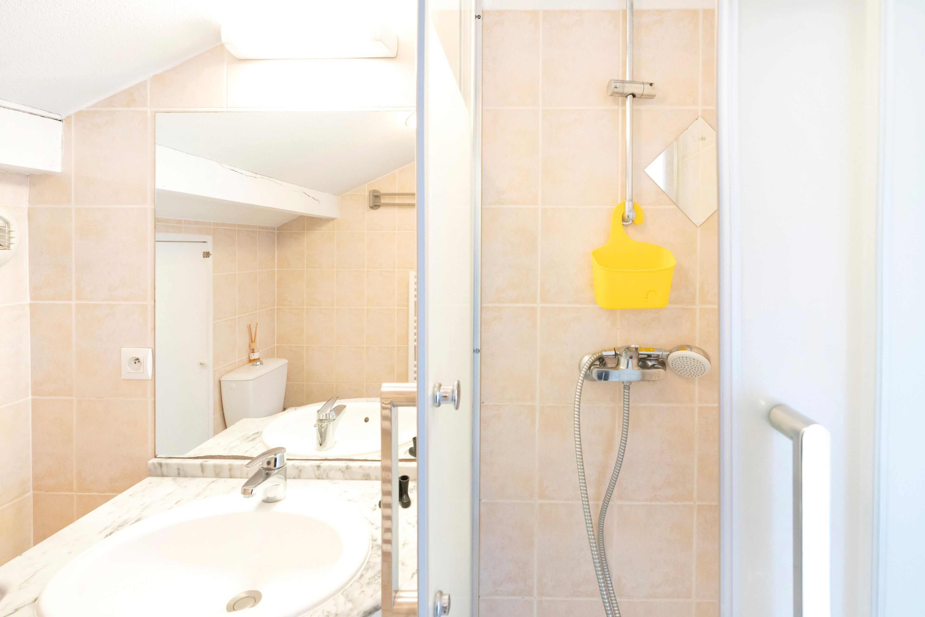 A bathroom with a sink, mirror, shower, and yellow bath mat.