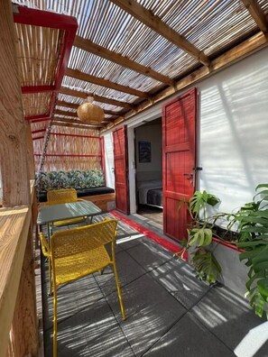 A covered outdoor seating area with a table and chairs, a door, and potted plants.