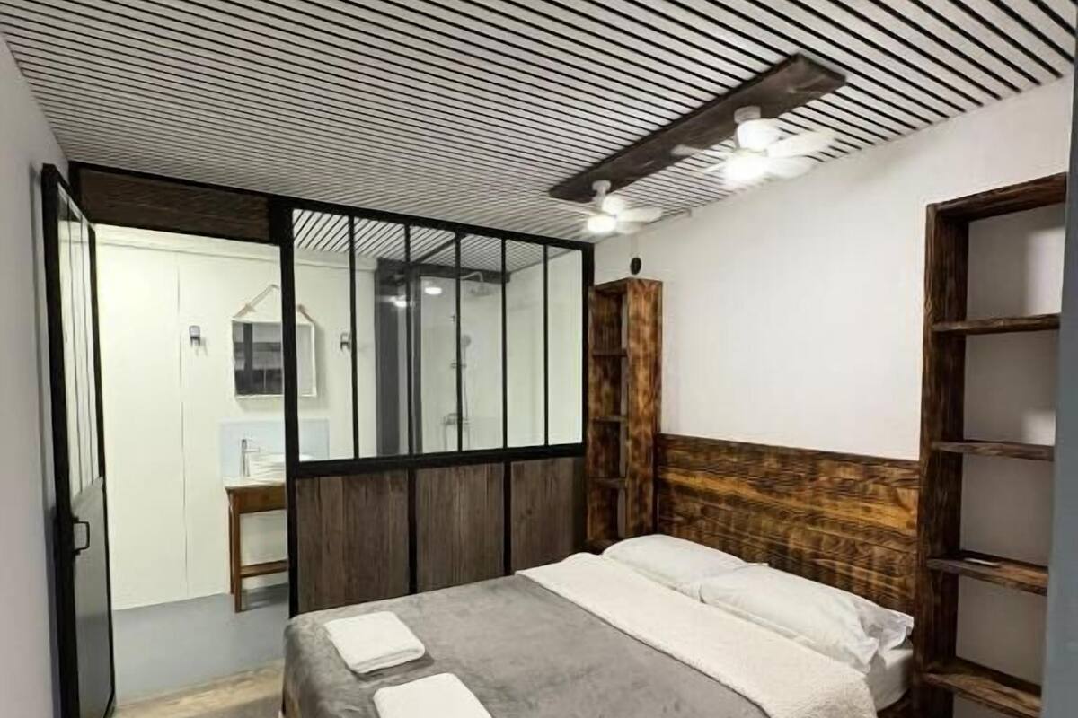 A modern bedroom with a slatted ceiling, a wooden headboard, and a large bed with a grey and white duvet.