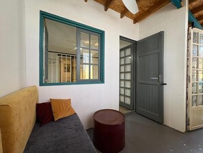 A room with a sofa, a round table, a window with a blue frame, and a door.