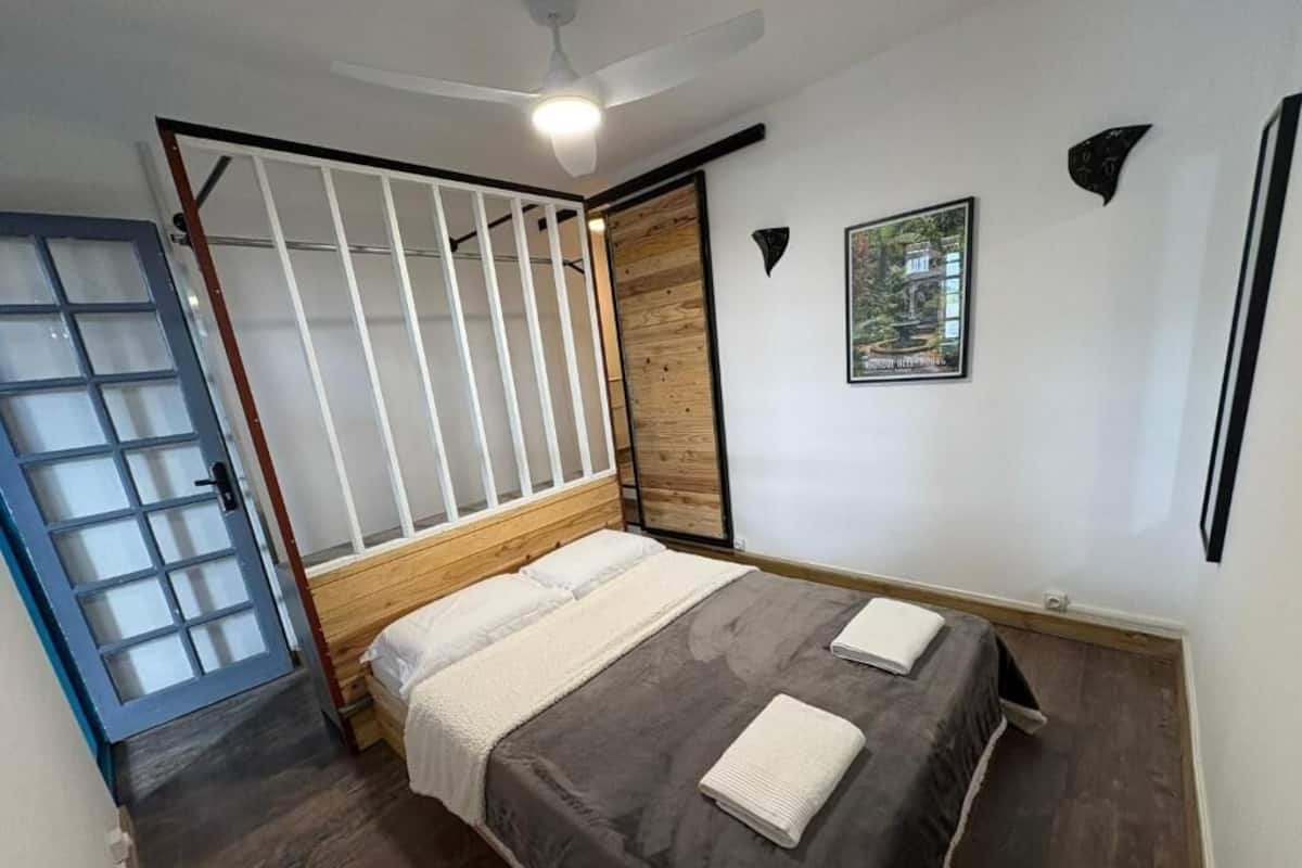 A bedroom with a bed, a wooden door, a white ceiling fan, and a framed picture on the wall.