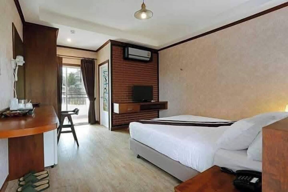 A hotel room with a bed, a desk with a chair, a television, and a window with curtains.