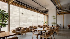 Et moderne spiseområde med træborde og stole, store vinduer med persienner og plantekasser.
