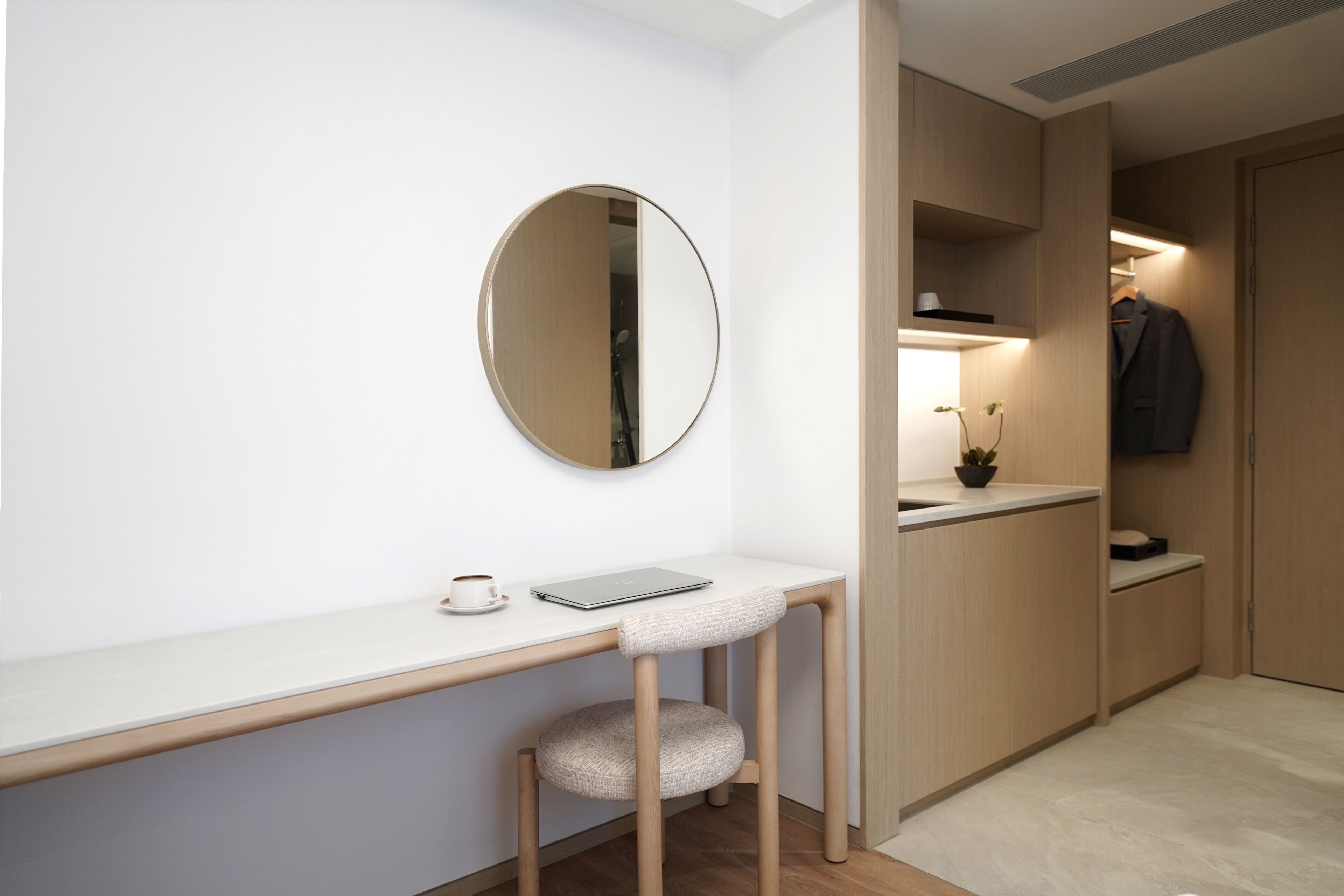 A modern, minimalist room with a white desk, a round mirror, a laptop, and a cup of coffee.