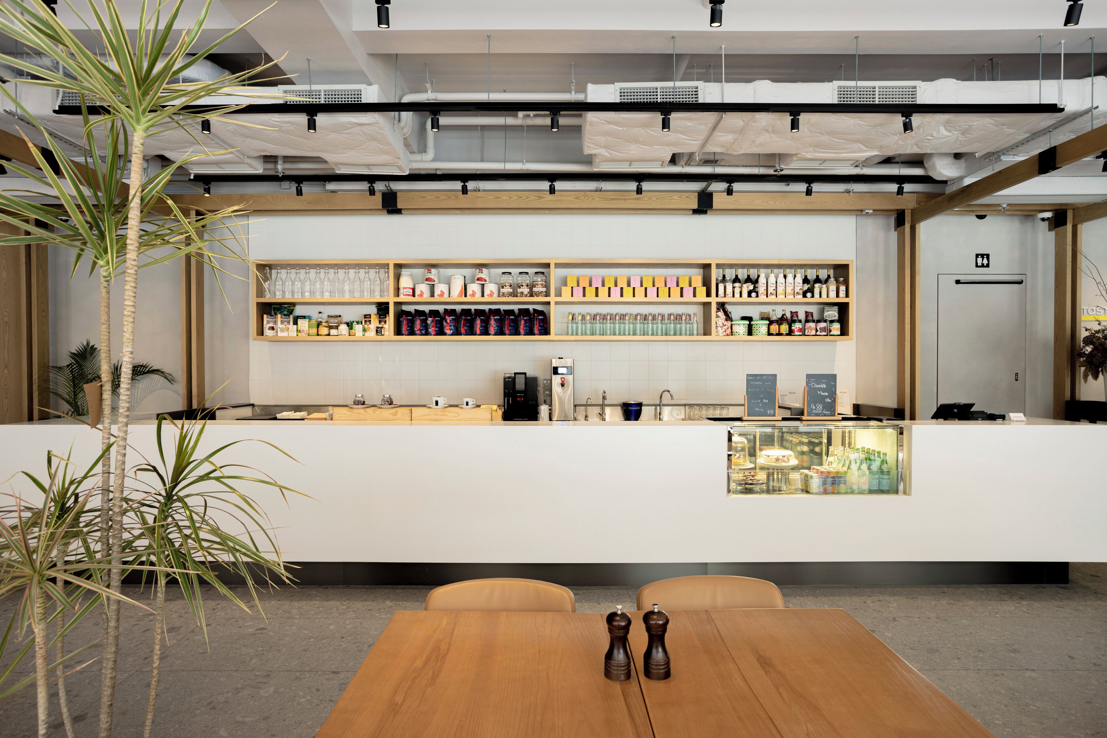 A modern bar area with a wooden counter, shelves stocked with bottles, and a coffee machine.