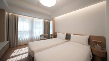 Habitación de hotel con dos camas, un escritorio, una silla y un ventanal con cortinas.