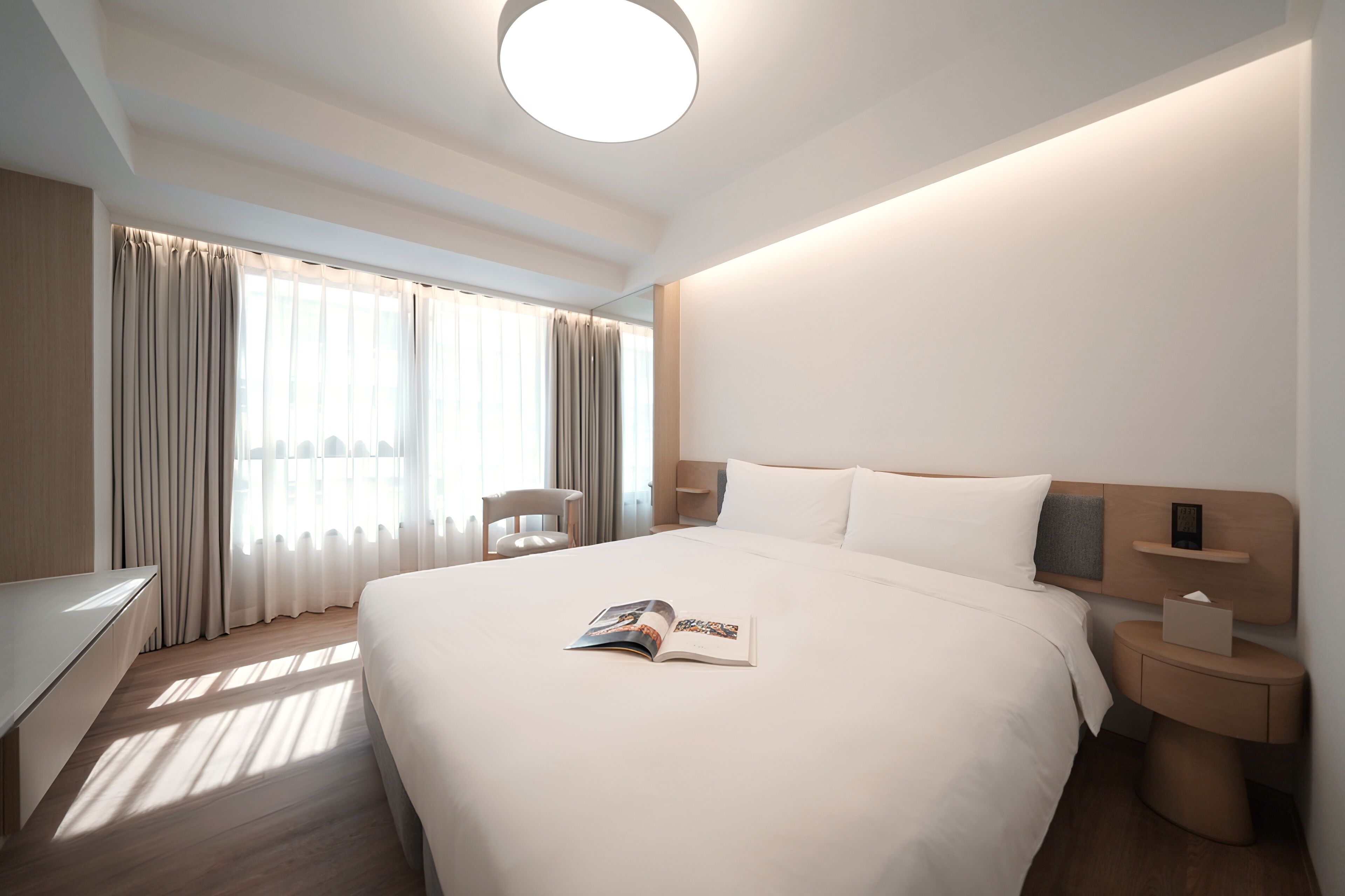 A modern hotel room with a large bed, bedside tables, a desk, and a chair.
