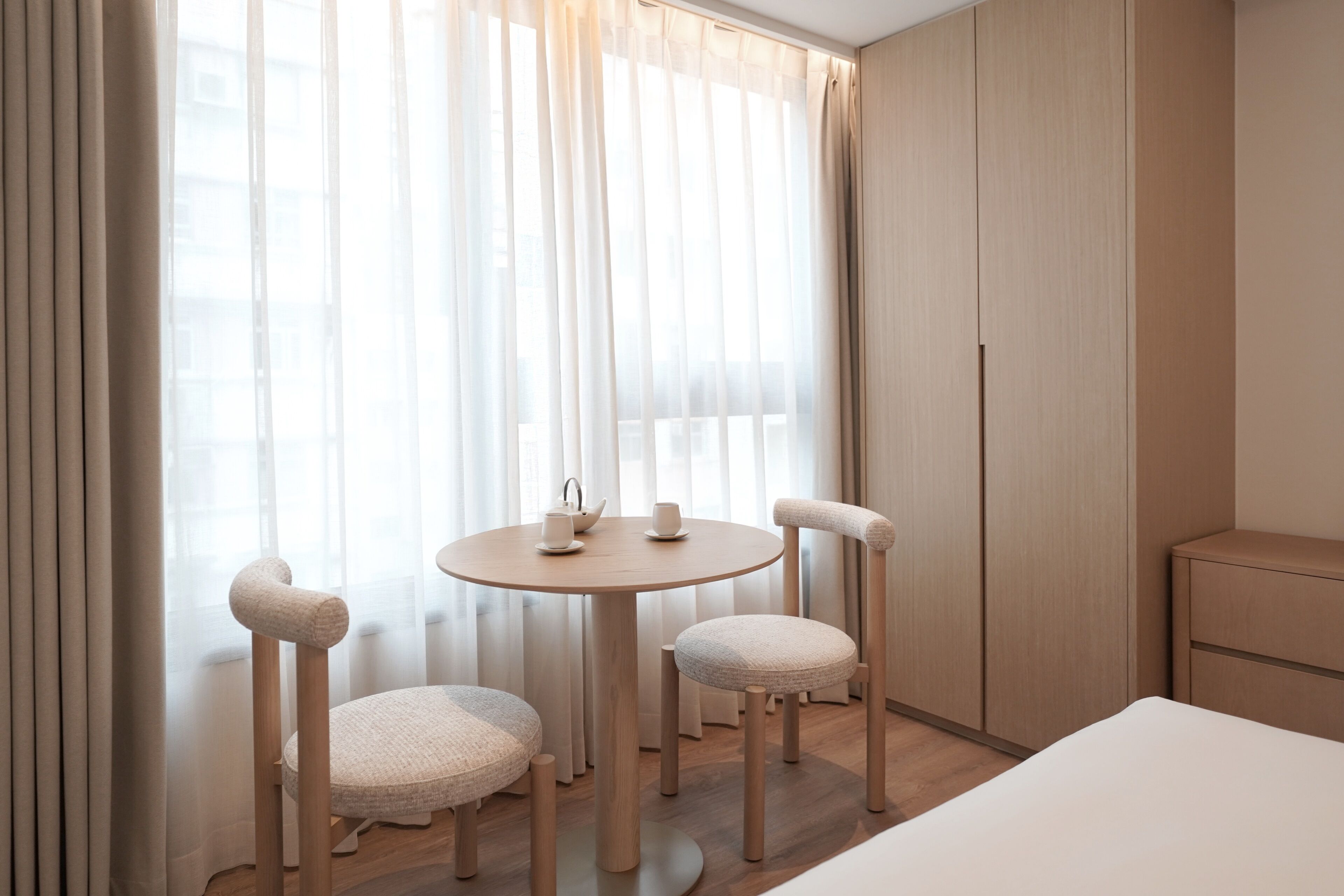 A hotel room with a round wooden table, two upholstered chairs, a bed, and a wardrobe.
