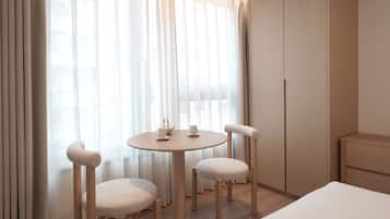 A hotel room with a round wooden table, two upholstered chairs, a bed, and a wardrobe.