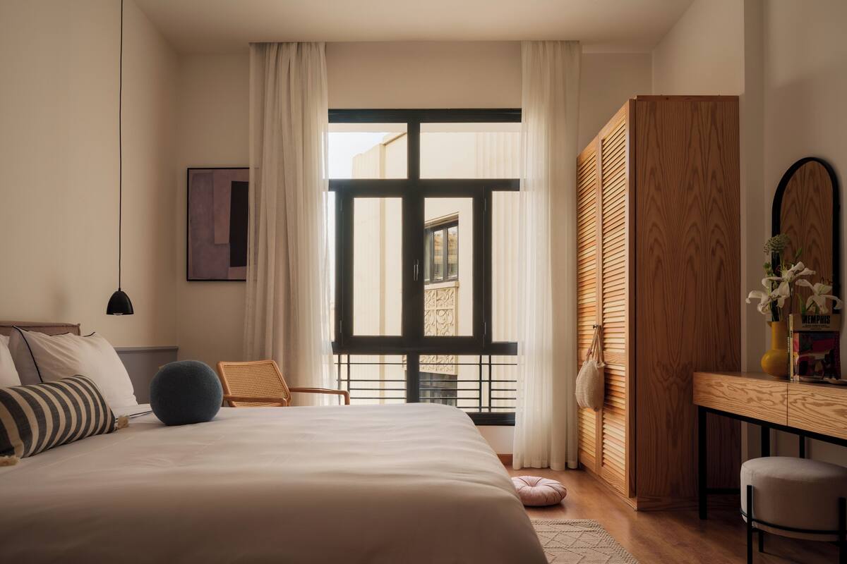 Une chambre à coucher avec un grand lit, un bureau, une chaise et une vue par la fenêtre.