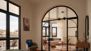Une chambre d’hôtel moderne dotée d’une grande fenêtre en arc de cercle, d’un lit, d’un coin salon avec un canapé et des fauteuils, et d’une petite table.