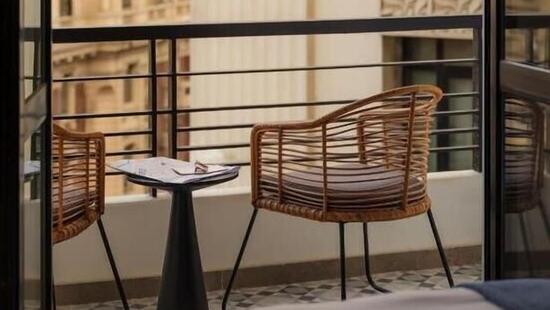 Un balcon avec deux fauteuils en osier et une petite table, d’où l’on peut admirer une vue sur la ville, avec ses bâtiments à l’architecture classique.
