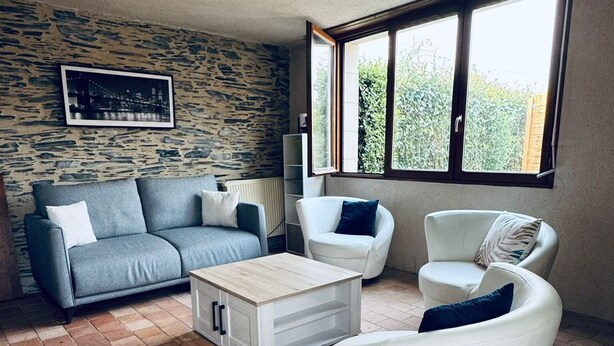 A living room with a stone wall, a grey sofa, a white armchair, and a coffee table. - Gîte 6 people 15min from Angers (Loire-Authion)