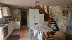 A compact kitchen with a dining table, chairs, and a staircase leading to an upper level. - Gîte 6 people 15min from Angers (Loire-Authion)