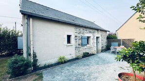 A two-story house with a stone facade and a grey roof. There is a small garden with a table and chairs outside. - Gîte 6 people 15min from Angers (Loire-Authion)
