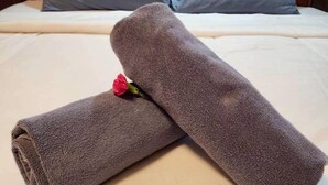 Cama bem arrumada com duas almofadas, uma toalha enrolada e uma flor.