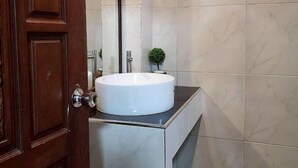 Uma casa de banho com porta de madeira, lavatório branco, uma pequena planta em vaso e paredes revestidas a azulejos.