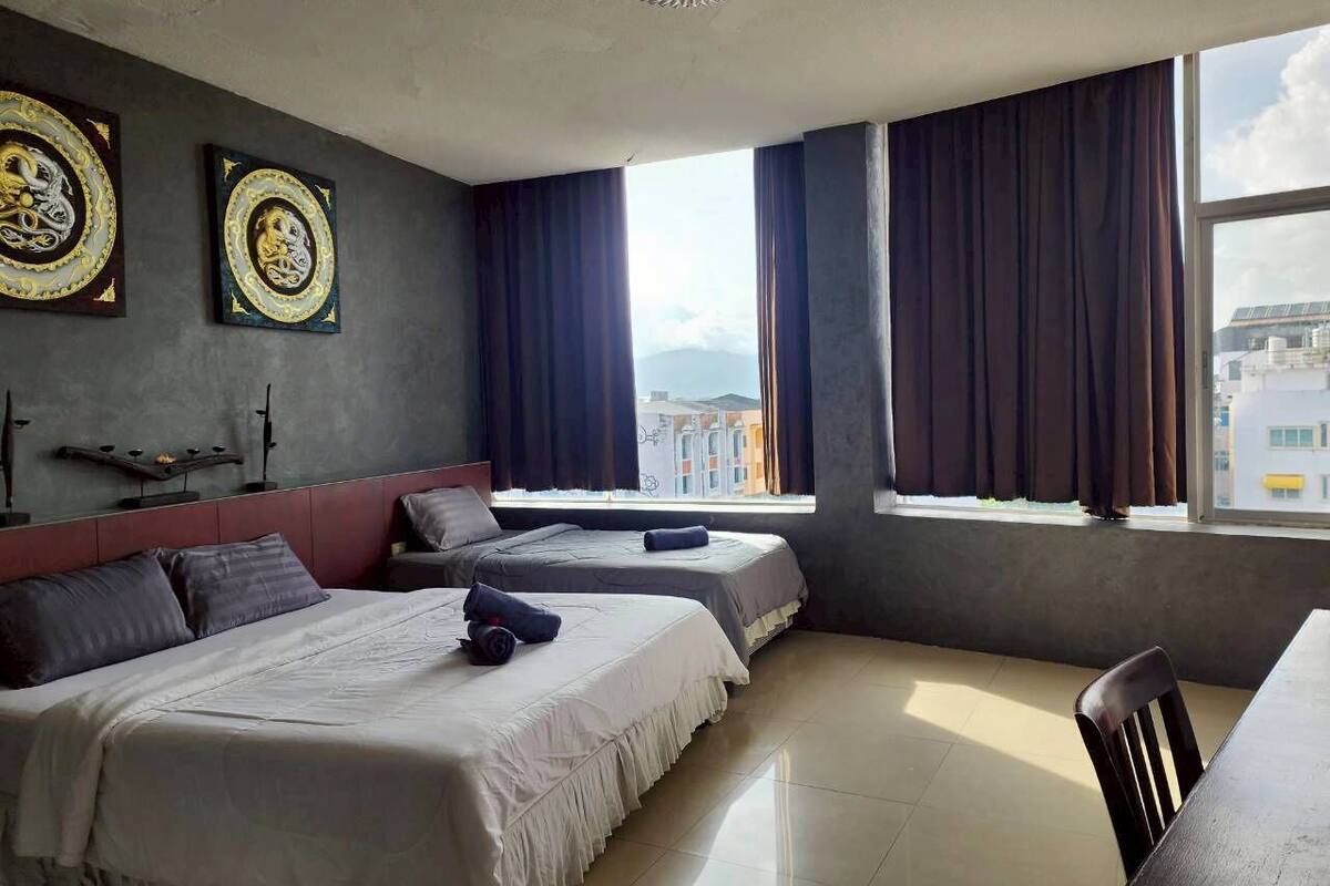 A hotel room with two beds, a dining table, and a large window with curtains.