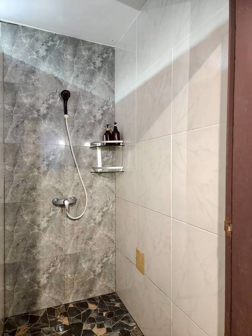 Baño con zona de ducha que presenta una pared de mármol y suelo de baldosas.
