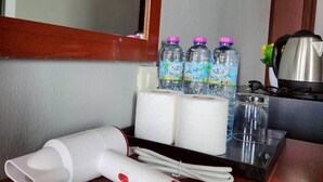 Quarto de hotel com uma mesa de madeira, secador de cabelo, água engarrafada e papel higiênico.