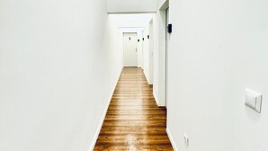 Un largo y estrecho pasillo con paredes blancas y piso de madera, que conduce a varias puertas.