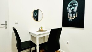 Una habitación pequeña con pared blanca, suelo de madera, una mesa blanca con una silla negra, un espejo redondo y una obra de arte blanco y negro.