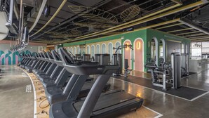 A gym with treadmills, weight machines, and a green wall with arched windows. - yangjiangshibailiyichengjiudian  (Yangjiang)