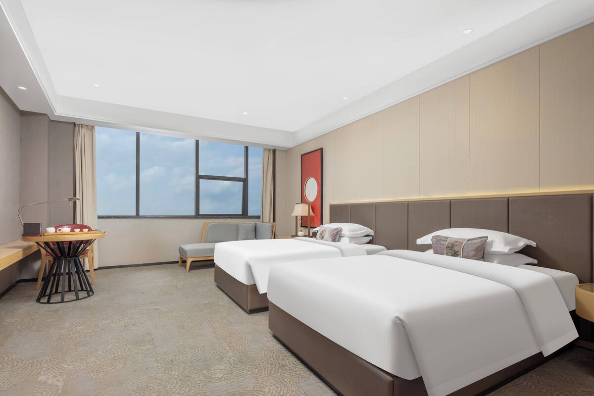 Ein Hotelzimmer mit zwei Betten, einem Schreibtisch, einem Stuhl und einem großen Fenster.