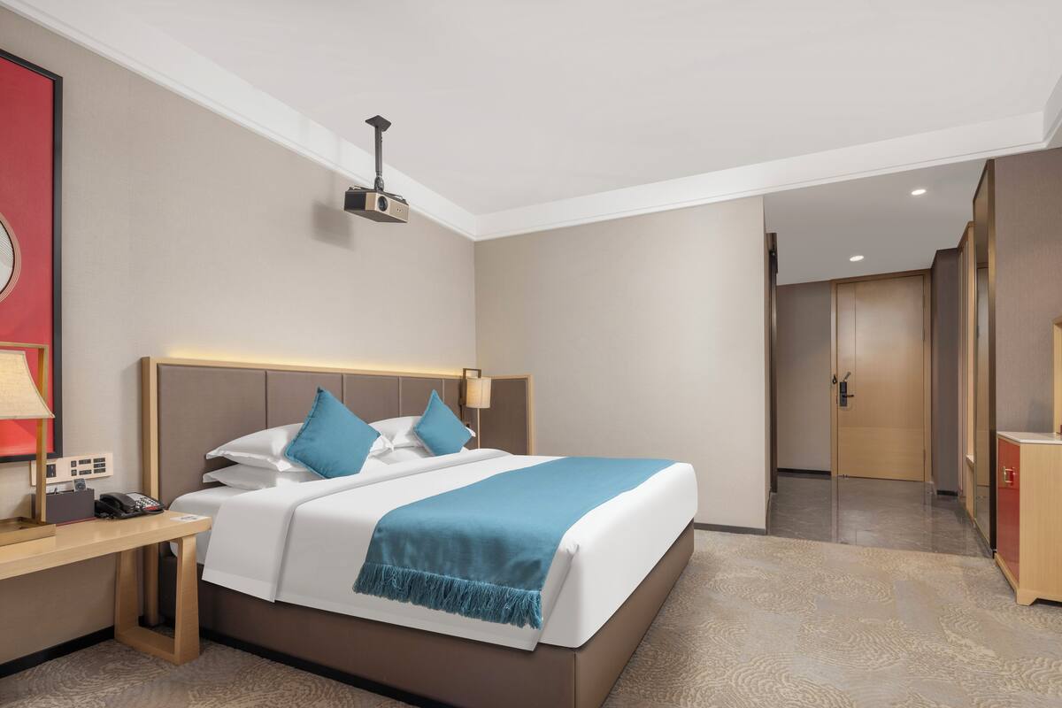Ein Hotelzimmer mit Bett, Nachttisch, Lampe und einer Deckenprojektion.