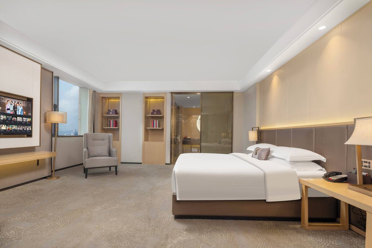 Ein Hotelzimmer mit einem großen Bett, einem Schreibtisch, einem Sessel, einem Fernseher und einem Kleiderschrank.