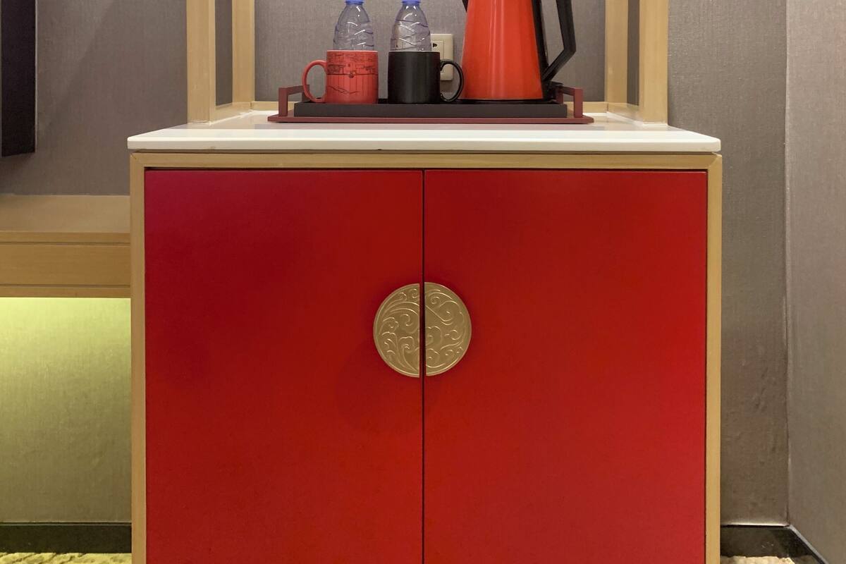 Ein roter Schrank mit einer kleinen Pflanze obenauf, zwei Wasserflaschen, eine rote Tasse und eine schwarze Tasse.