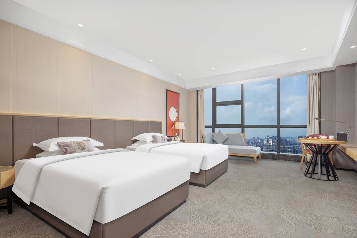 Ein Hotelzimmer mit zwei Betten, einem Schreibtisch und Blick auf die Stadt.