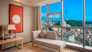 A modern hotel room with a large window offering a city view, a sofa, a desk with a lamp, and a framed picture on the wall. - yangjiangshibailiyichengjiudian  (Yangjiang)
