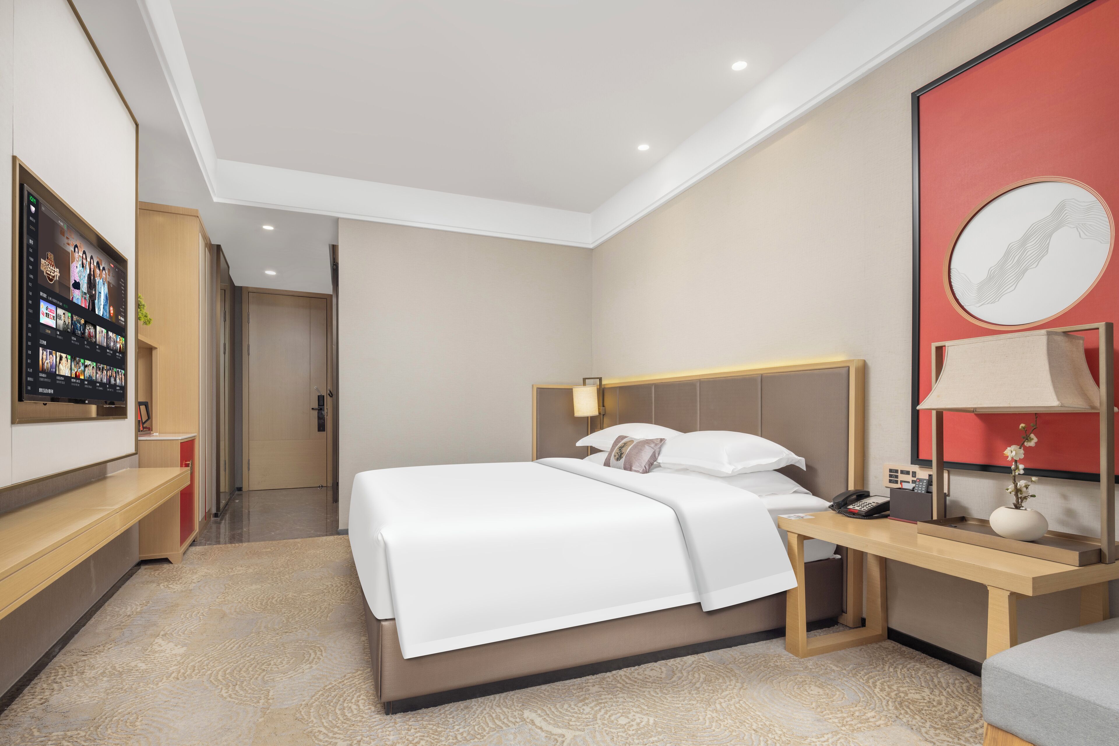 Quarto de hotel moderno com cama grande, mesa de cabeceira, abajur e televisão presa na parede.