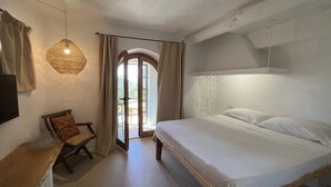 A bedroom with a large bed, a wooden nightstand, a chair, and a hanging light fixture. - DomoMea Porto Cervo (Arzachena)