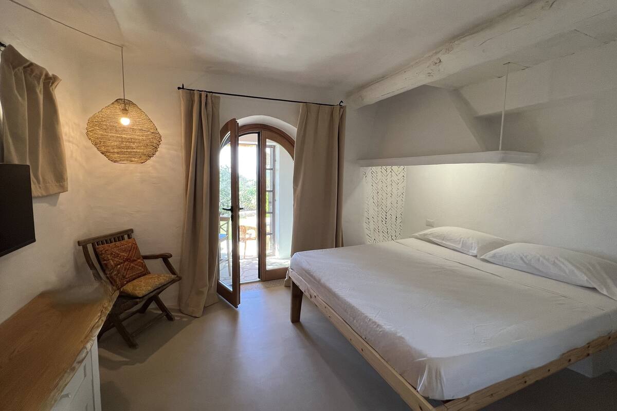 A bedroom with a large bed, a wooden nightstand, a chair, and a hanging light fixture.
