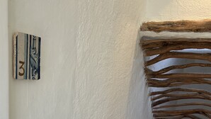A staircase with a textured white wall, a wooden handrail, and a small shelf with a decorative item. - DomoMea Porto Cervo (Arzachena)