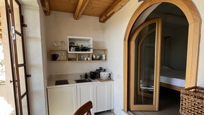 A compact kitchen with white cabinets, a wooden dining table, and a large window. - DomoMea Porto Cervo (Arzachena)