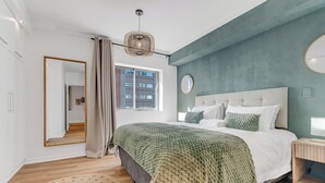 A modern bedroom with a large bed, a mirror, a window, and a wooden bedside table. - Modern apartment with skyline and sea views (Cape Town)