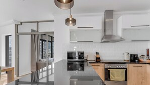 A modern kitchen with a large island, stainless steel appliances, and a view to the outside. - Modern apartment with skyline and sea views (Cape Town)